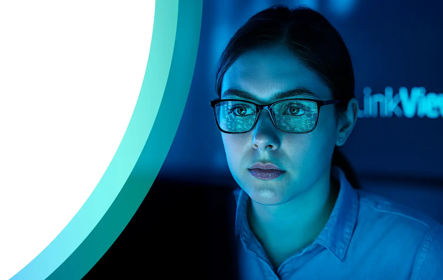 Femme portant des lunettes observant un écran d’ordinateur avec reflets de données dans une lumière bleue