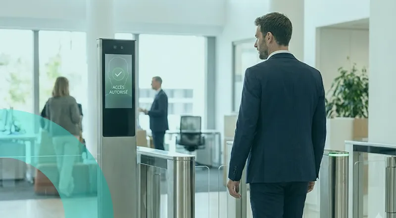 Environnement de bureau avec un contrôle d’accès : un homme se présente devant des portiques, avec un écran affichant une reconnaissance faciale.
